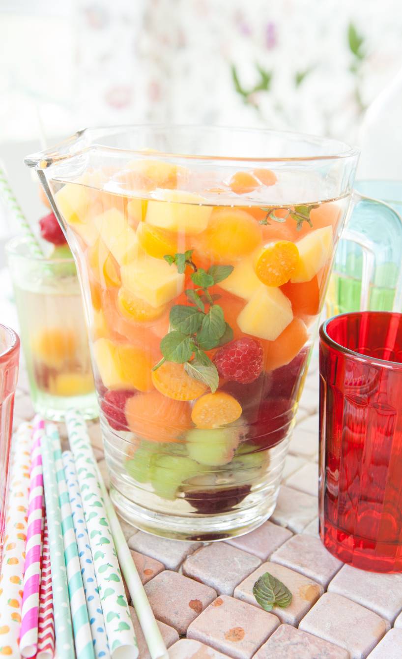 Bowle in einer Karaffe voll mit Früchten auf einem Gartentisch, daneben Papierstrohhalme