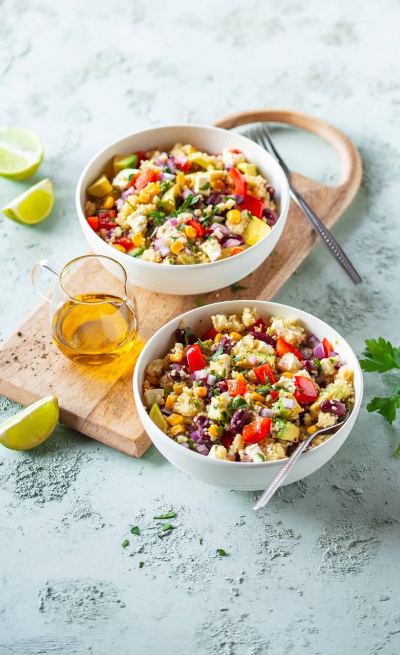 Couccous-Salat in zwei Salatschüsseln mit Avocado und Feta getoppt, daneben Dressing
