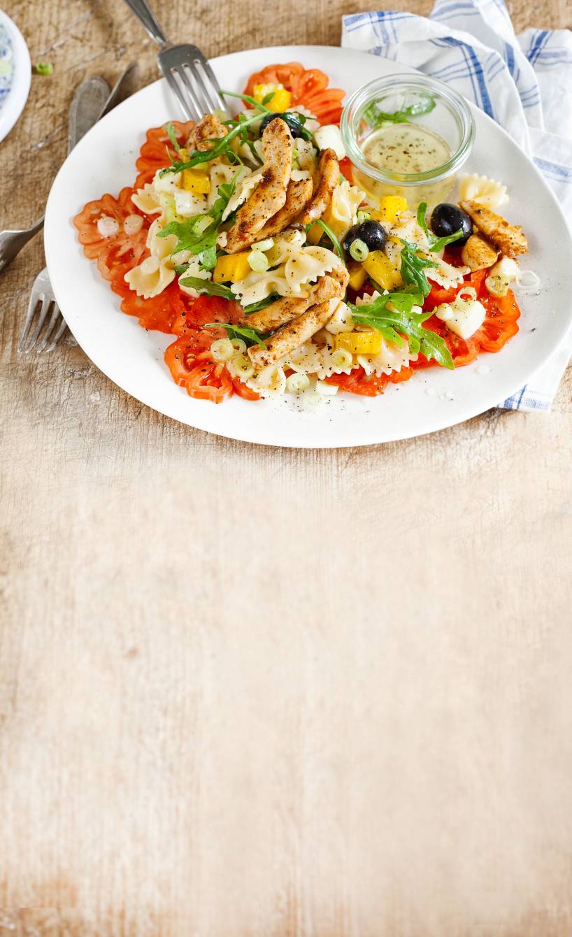 Nudelsalat getoppt mit Hähnchentreifen und Mozzarella auf einem Tisch