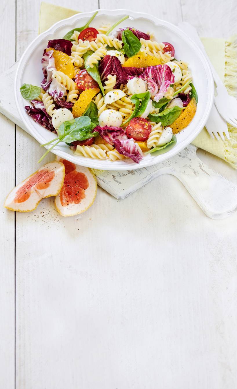 Nudelsalat aus Fusilli , Spinat und Tomaten in einer Schüssel getoppt mit Mozzarellakugeln und Grapefruitstücken auf einem Tisch