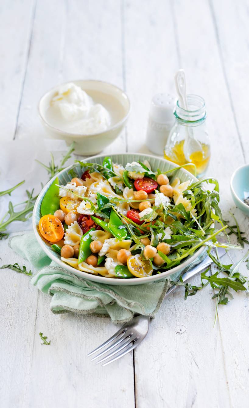 Pastasalat aus Fusilli in einer Salatschüssel getoppt mit Mozzarella und Kichererbsen auf einem Tisch