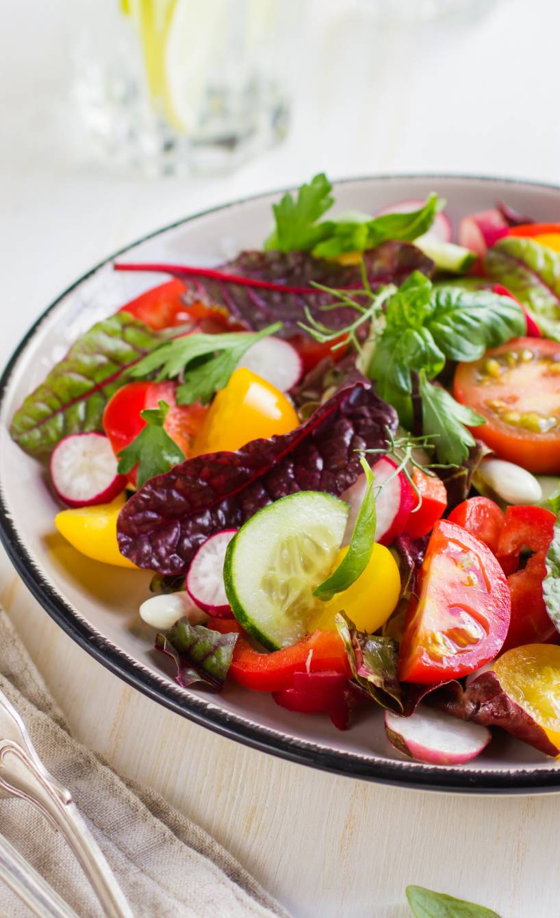 Bunter Mangold-Salat in einer Schüssel, daneben eine Wasserkaraffe auf einem Tisch