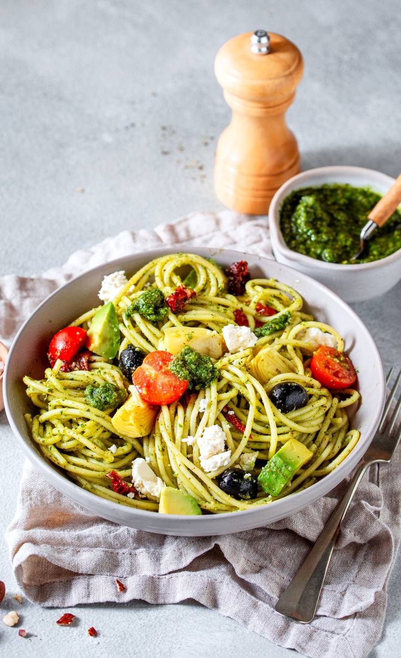 Spaghettisalat auf einem tiefen Teller, daneben eine Schale mit Bärlauchpesto und eine Pfeffermühle