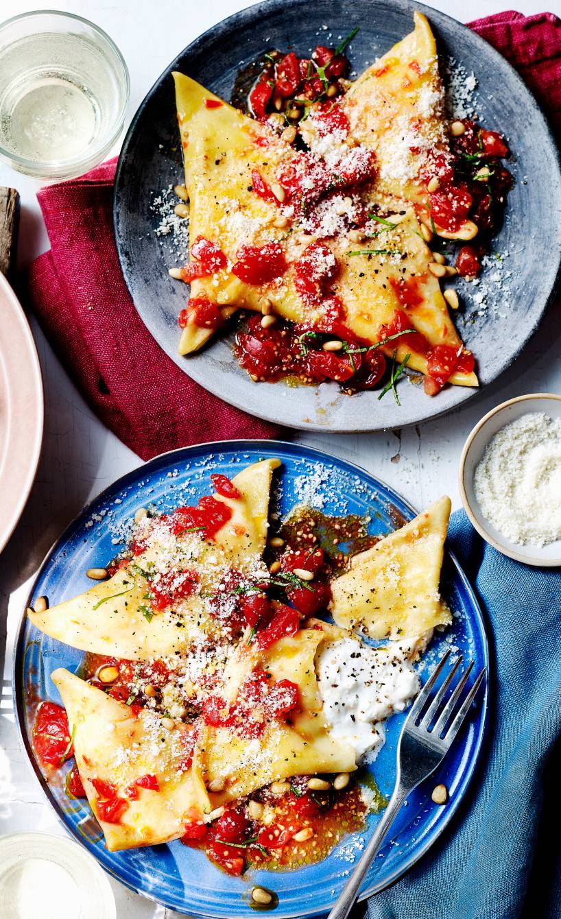 Dreieckige Pansotti auf mehreren Tellern, Füllung aus geschmolzenem Burrata tritt heraus, darauf Kirschtomaten, Parmesan und Basilikum