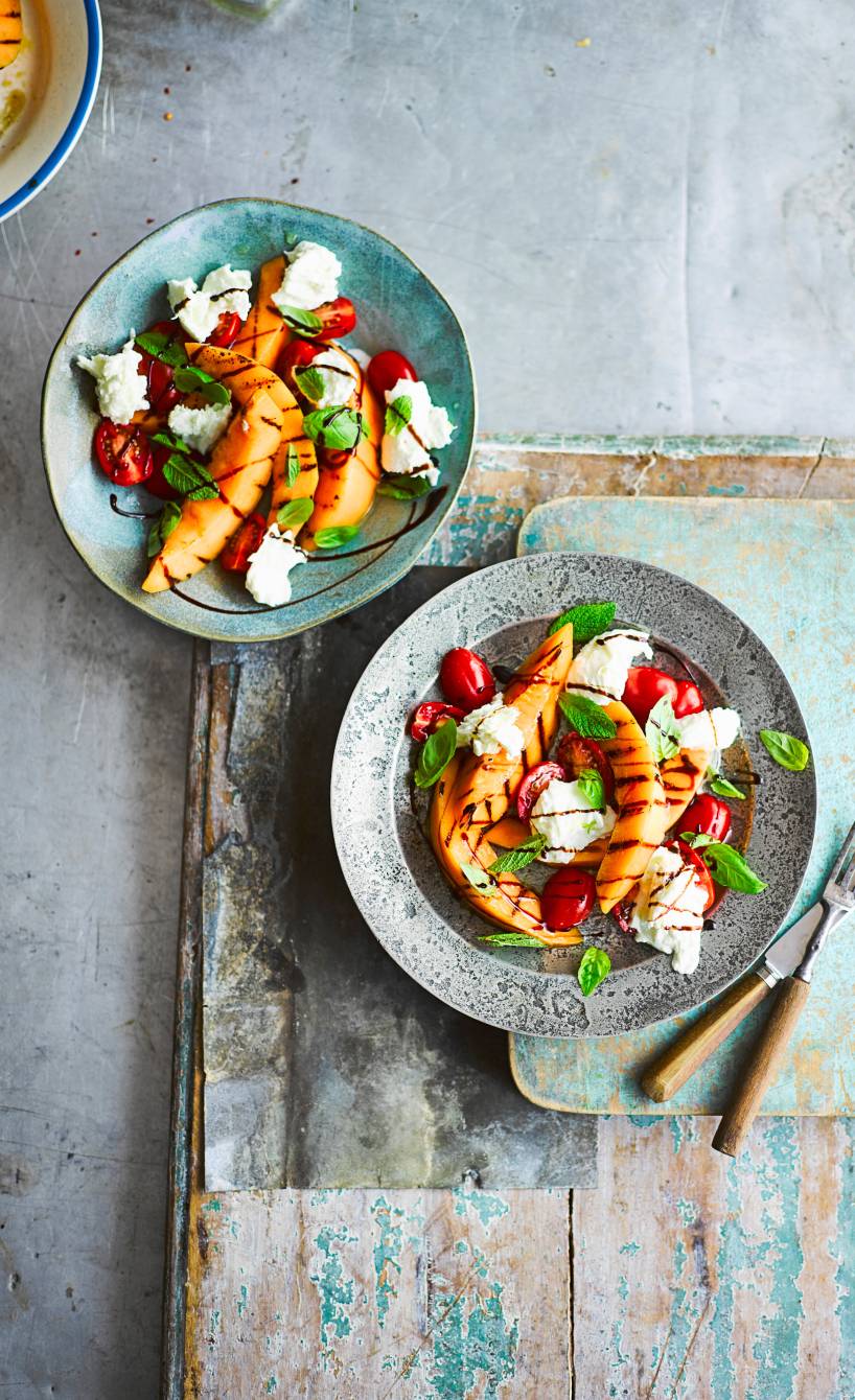 Caprese-Salat in zwei Salattellern getoppt mit Mozzarella und gegrillter Melone auf einem Tisch