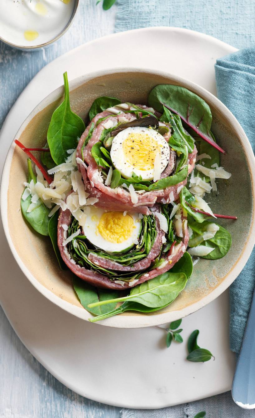 Zwei Rinderfilet-Carpaccio-Roulade gefüllt mit halbierten Eiern angerichtet auf Salatbetten auf zwei Tellern