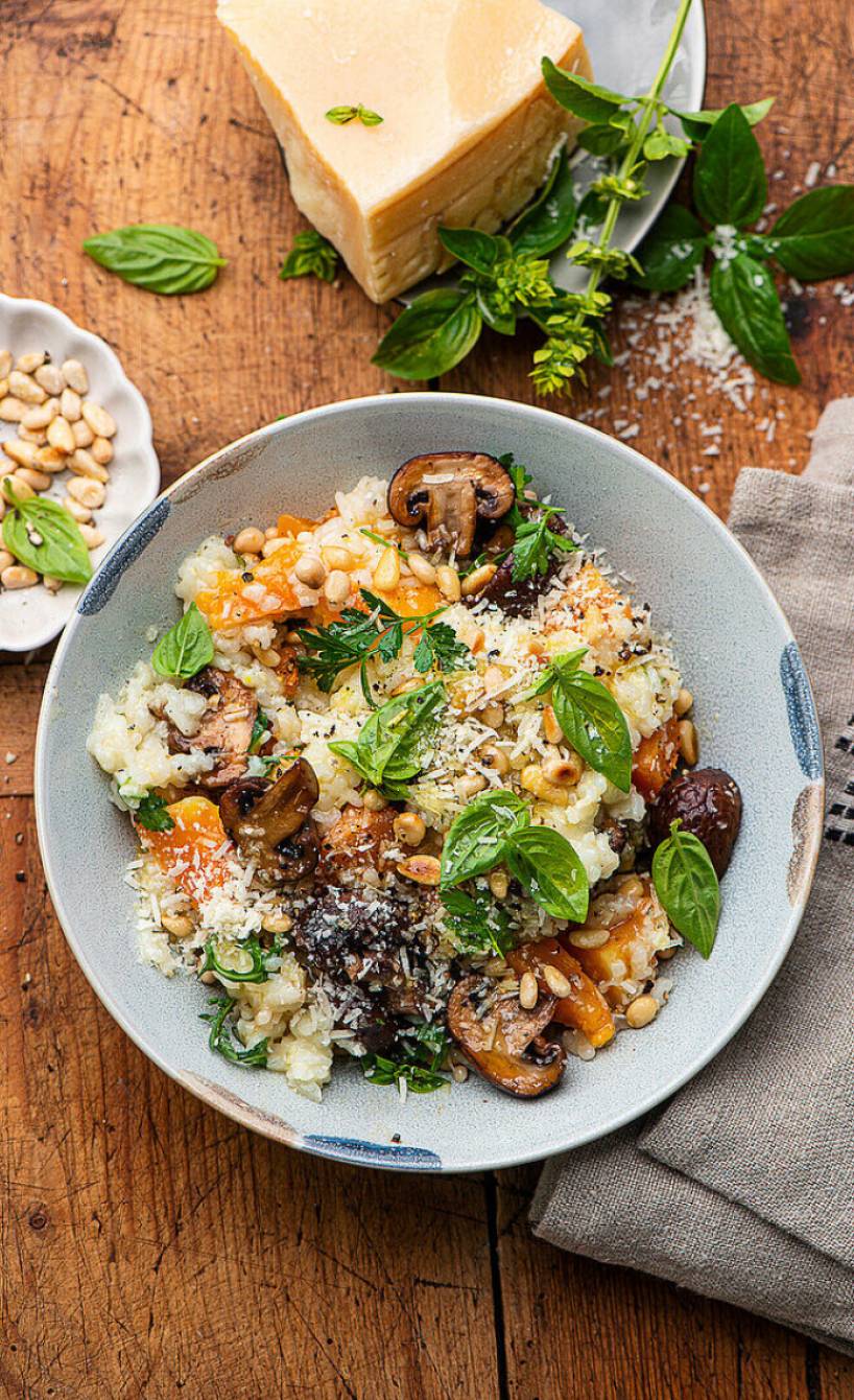 Selbstgekochtes Risotto mit Kürbis, Champignons und Rucola angerichtet auf einem tiefen Teller getoppt von Parmesan und Pinienkernen