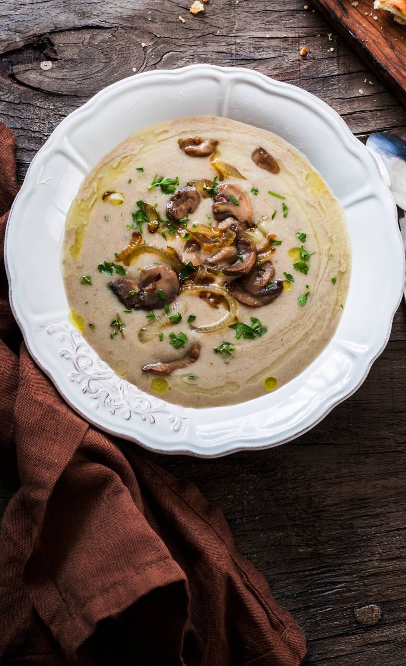 Selbst gekochte Champignoncremesuppe in einem Suppenteller garniert mit Pilzscheiben und Zwiebeln, daneben Ciabatta