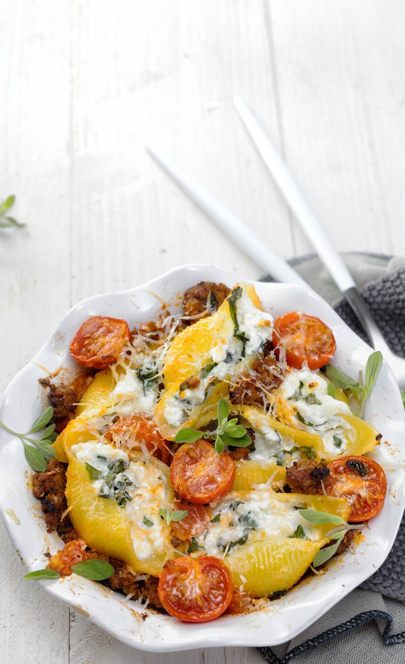 Gebackene Conchiglioni mit Ricotta-Füllung auf Hackfleischsoße in einer Auflaufform auf einem Tisch