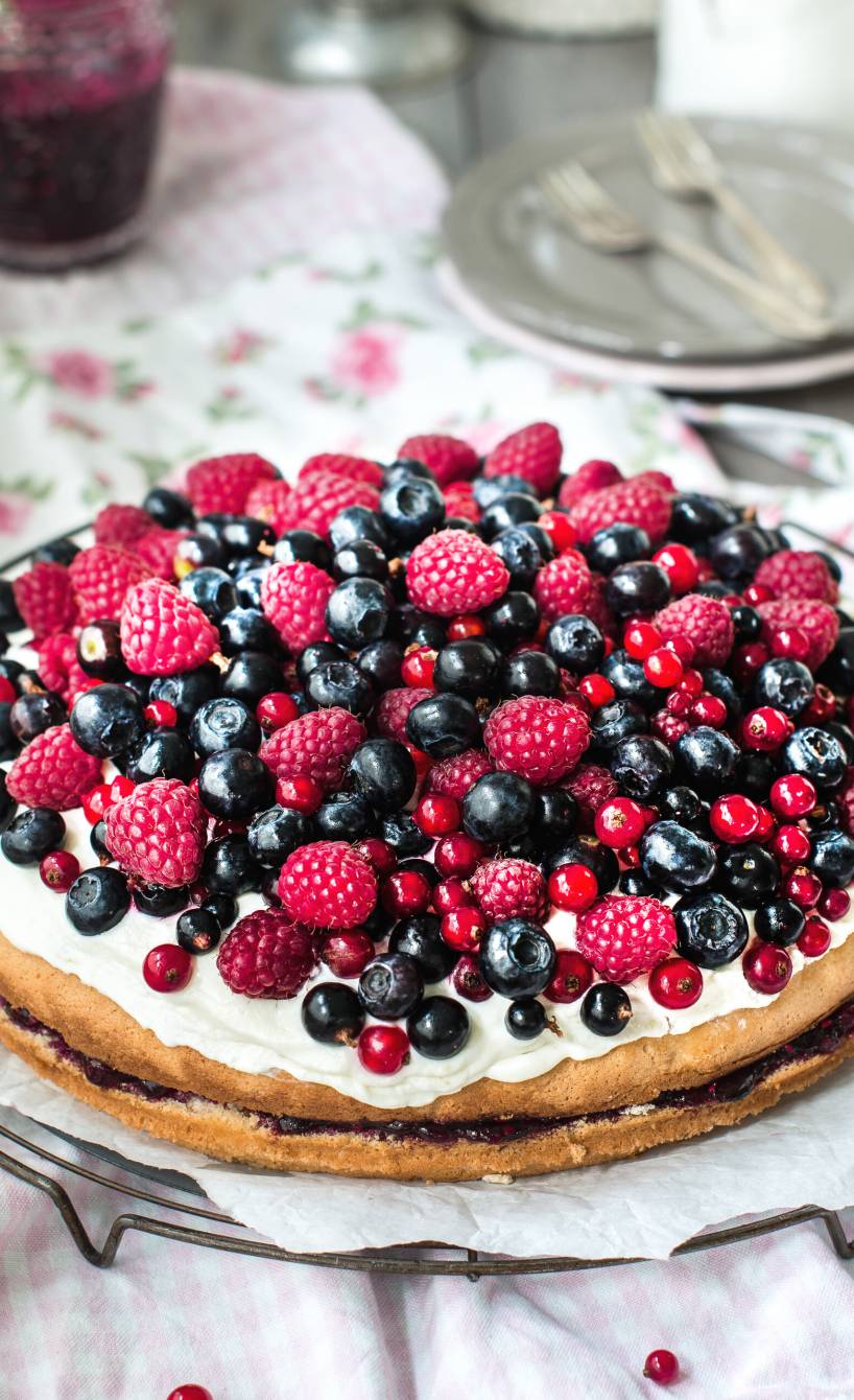Runde Beerentorte mit Biskuitboden und sahniger Quarkcreme-Füllung getoppt von frischen Beeren auf einer Tortenplatte
