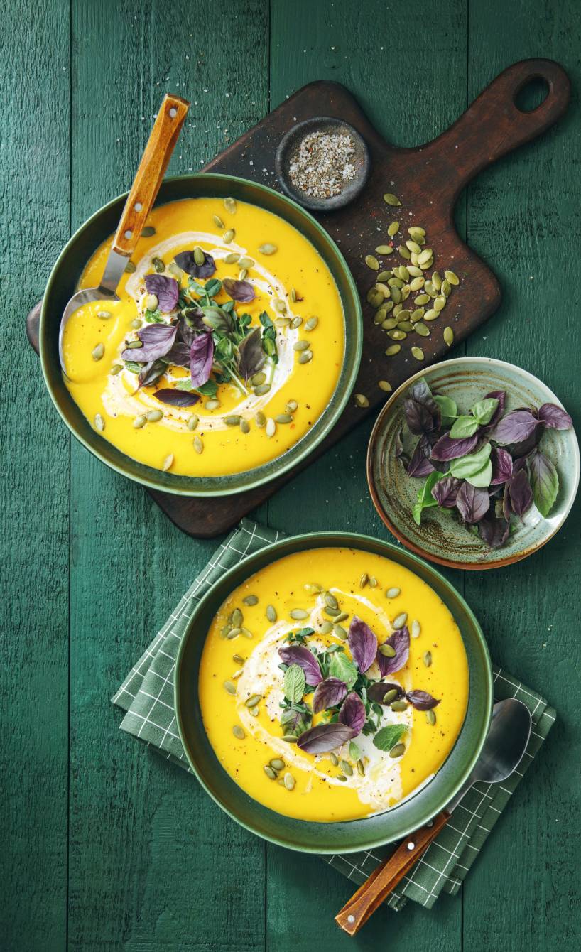 Kürbissuppe in zwei Suppenschüsseln auf einem Tisch getoppt mit frischen Kräutern und Kürbiskernen