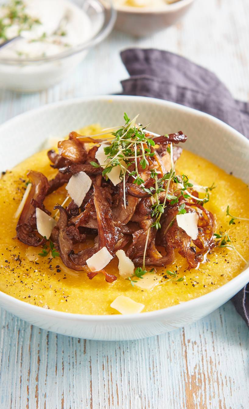 Polenta in einem tiefen Teller getoppt von gebratenen Austernpilzen und Parmesanspänen