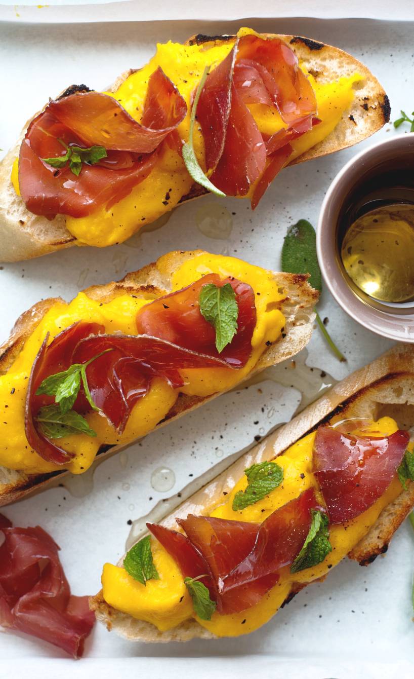 Crostini mit Kürbis und Bresaola belegt auf einem eckigen Teller