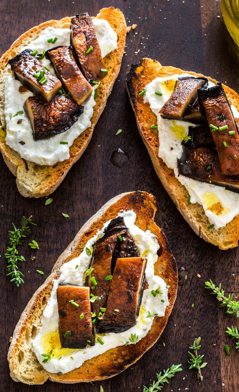 Drei Crostini mit Ricotta und gebratenen Steinpilzen auf einem Holzbrett