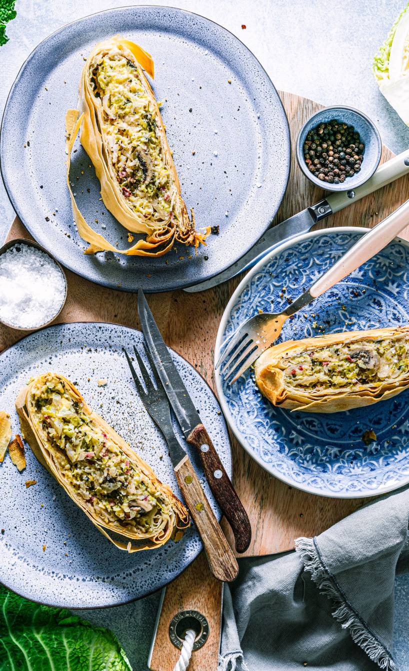 Drei Stücke Gemüsestrudel mit Wirsing, Champignons und Speck auf Tellern angerichtet
