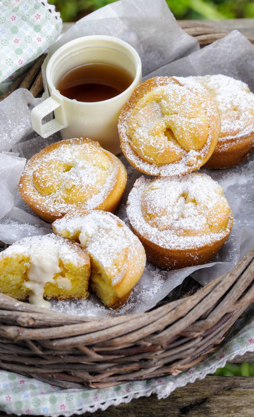 Poffertjes mit Eierlikör und weißem Schokokern in einem Weidenkorb draußen, daneben eine Kanne Tee