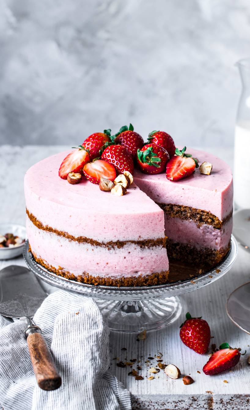 Glutenfreie, zweistöckige Erdbeer-Buttermilchtorte mit Nussboden dekoriert mit frischen Erdbeeren und Haselnüssen