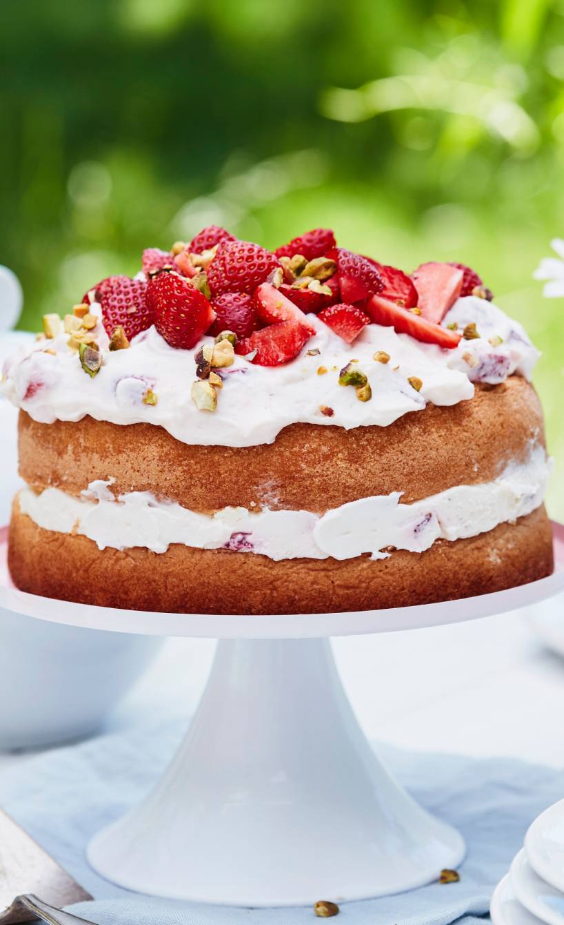 Mehrstöckige Erdbeer-Sahne-Torte mit einem Topping aus frischen Erdbeeren und Pistazien auf einer Tortenplatte