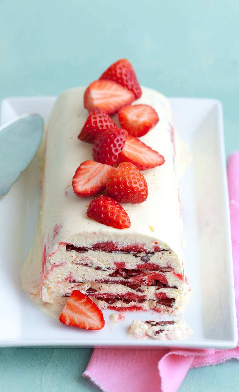 Semifreddo mit Erdbeeren angeschnitten auf einer Kuchenplatte garniert mit frischen Erdbeeren