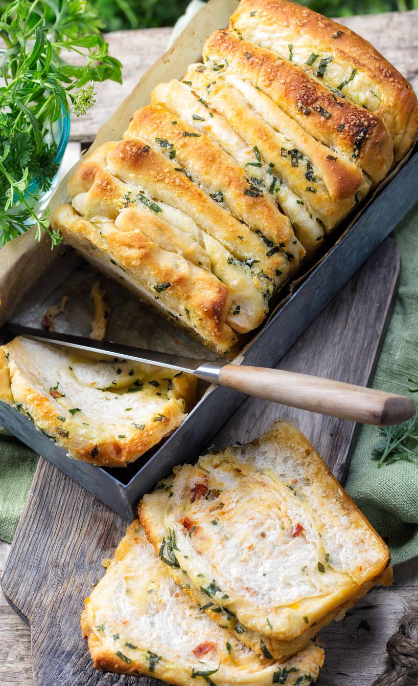Zupfbrot mit Bärlauch-Kräuterbutter in einer Kastenform, daneben ein paar Scheiben auf einem Teller