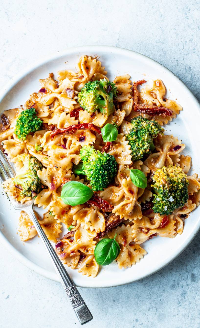 Farfalle mit Brokkoli, Pesto-Sahnesoße und getrockneten Tomaten auf einem Teller von oben