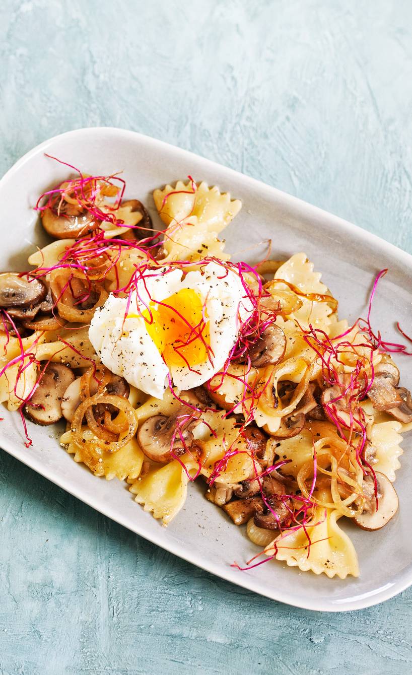 Gebratene Nudeln mit Champignons auf einem Teller getoppt von einem pochierten Ei mit weichem Kern