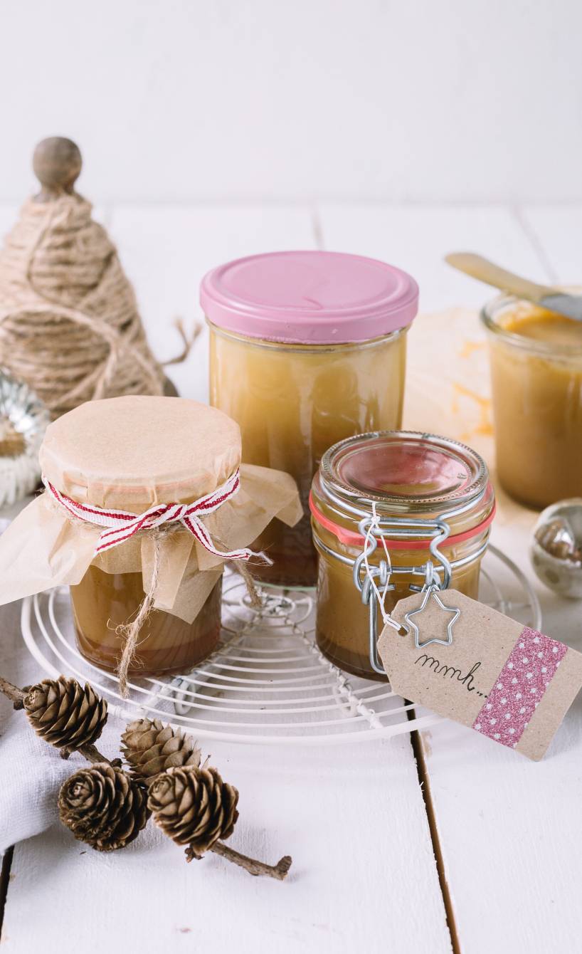 Selbst gemachte Karamellcreme in Gläser abgefüllt und als Geschenk verpackt auf einem Holztisch