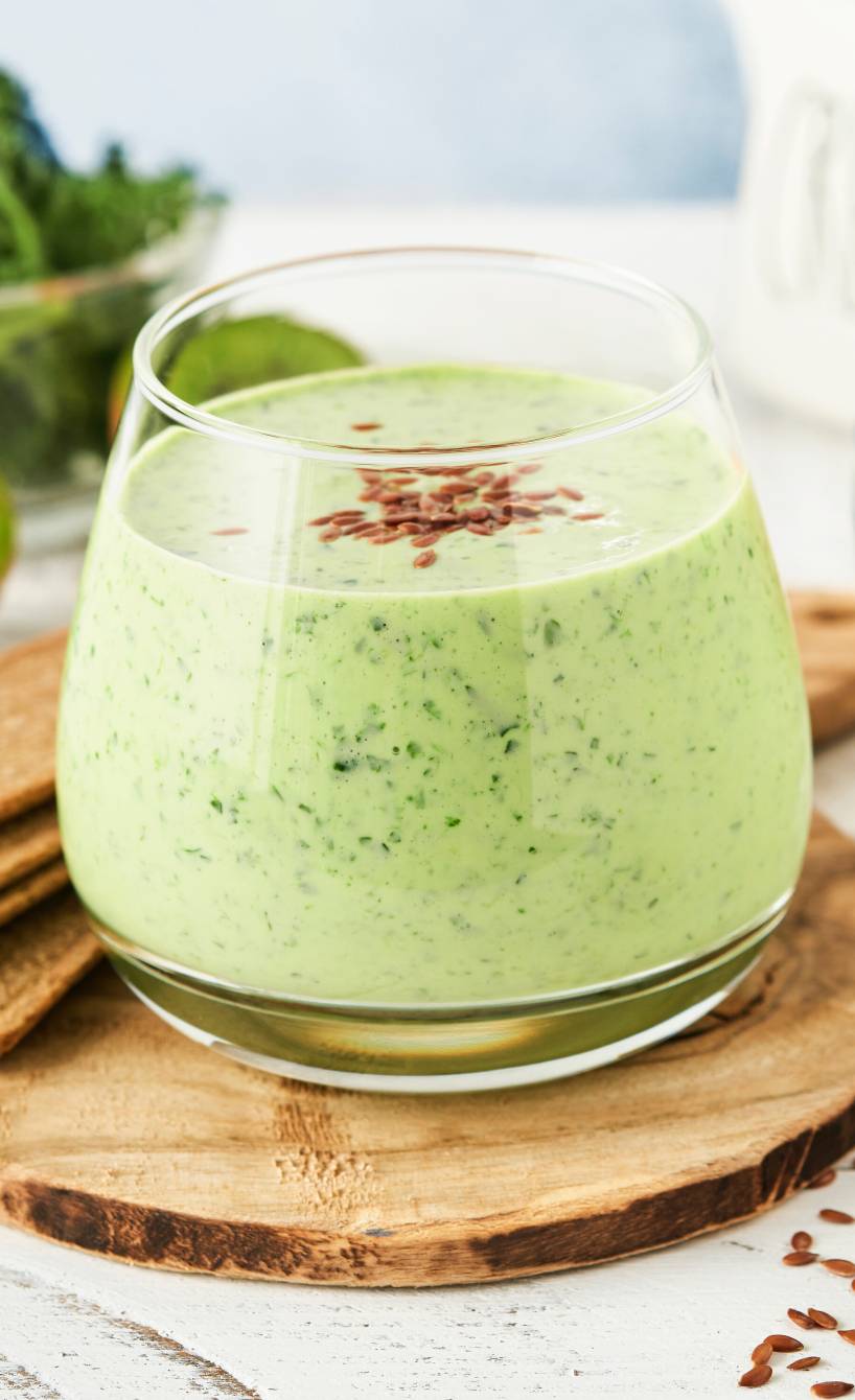Grüner Smoothie in einem Glas, daneben Spinat, Fenchel, Kiwi und Leinsamen auf einem Tisch