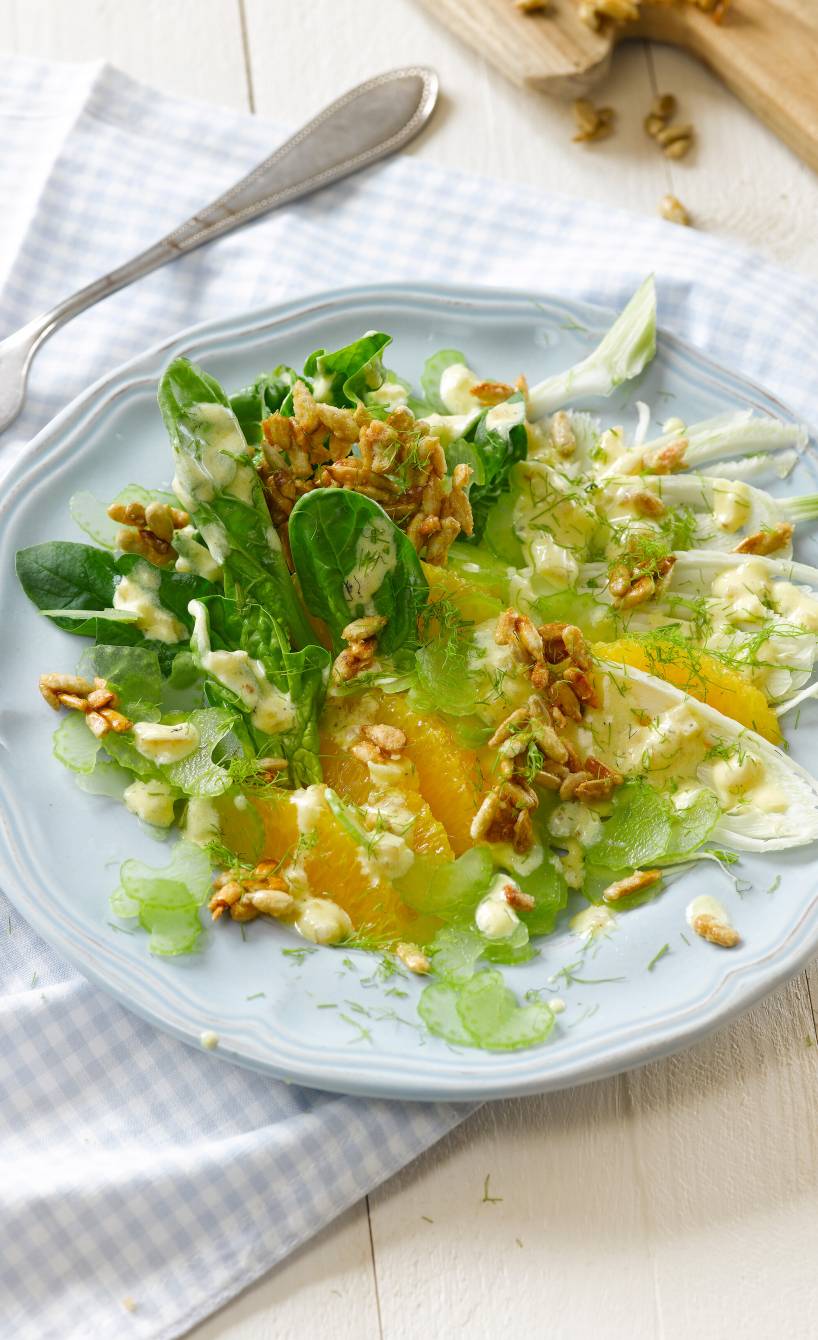 Spinat-Fenchelsalat getoppt von mit Orangen und karamellisieren Sonnenblumenkernen angerichtet auf einem Salattteller