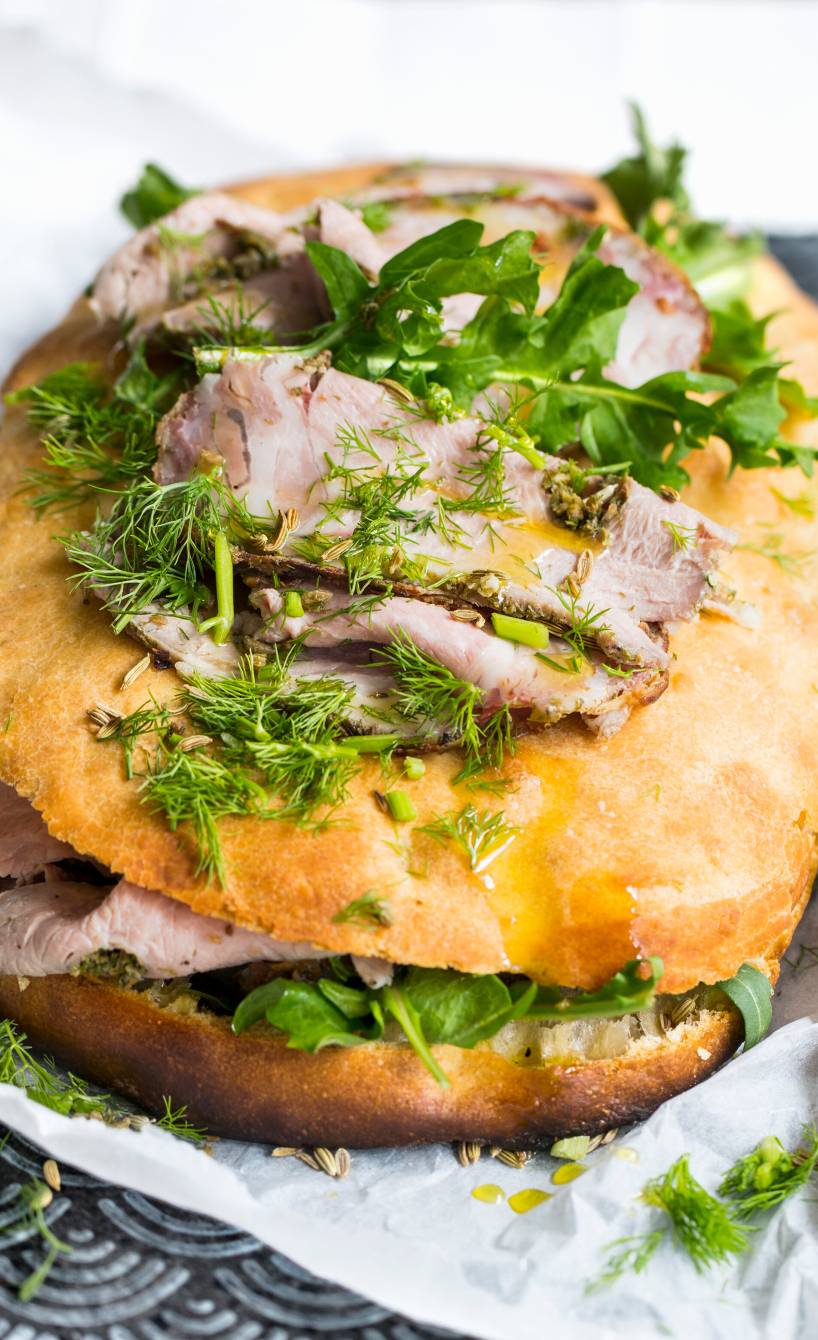 Gefülltes Focaccia mit Schweinebraten und belegt mit frischen Kräutern