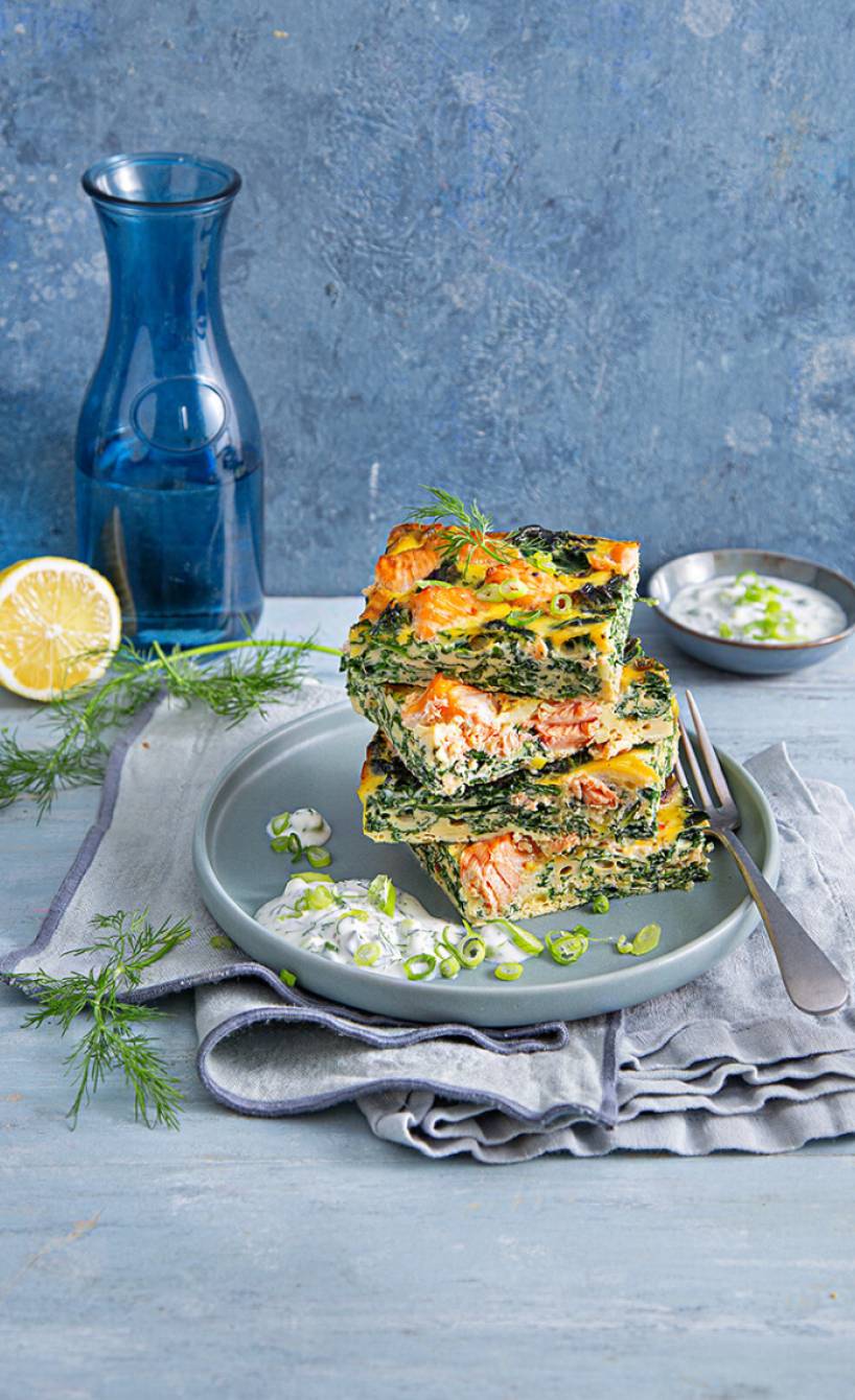 Grünkohl-Lachs-Frittata in Stücke geschnitten und gestapelt auf einem Teller, daneben Joghurt-Dill-Dip
