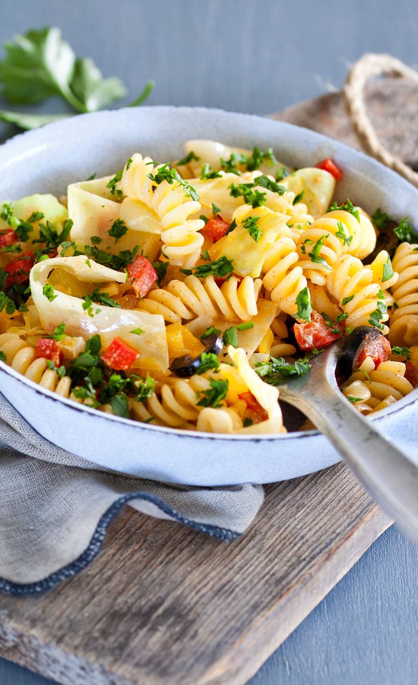 Pfanne mit Fusilli, Spitzkohl und anderem Gemüse auf einem Holzbrett