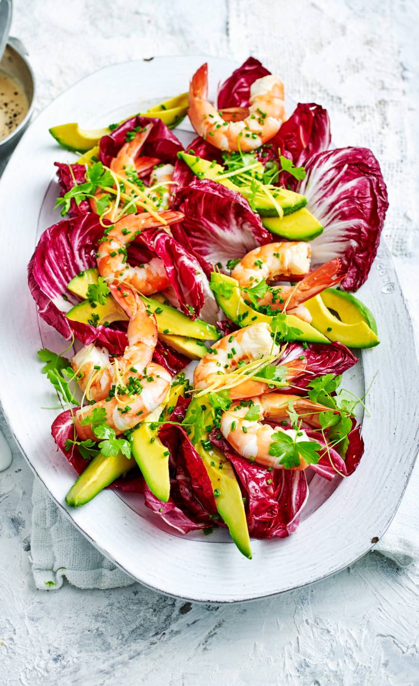 Radicchio-Avocado-Salat getoppt mit Garnelen angerichtet auf einer Servierplatte, daneben eine Schale mit Dressing
