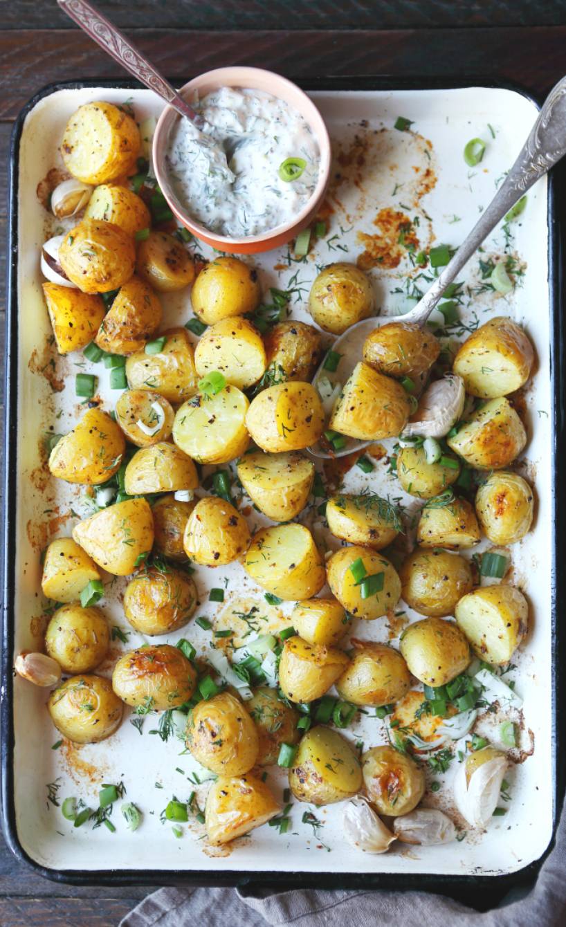 Ogengebackene Knoblauchkartoffeln auf einem Backblech, darauf eine Schale Joghurtdip