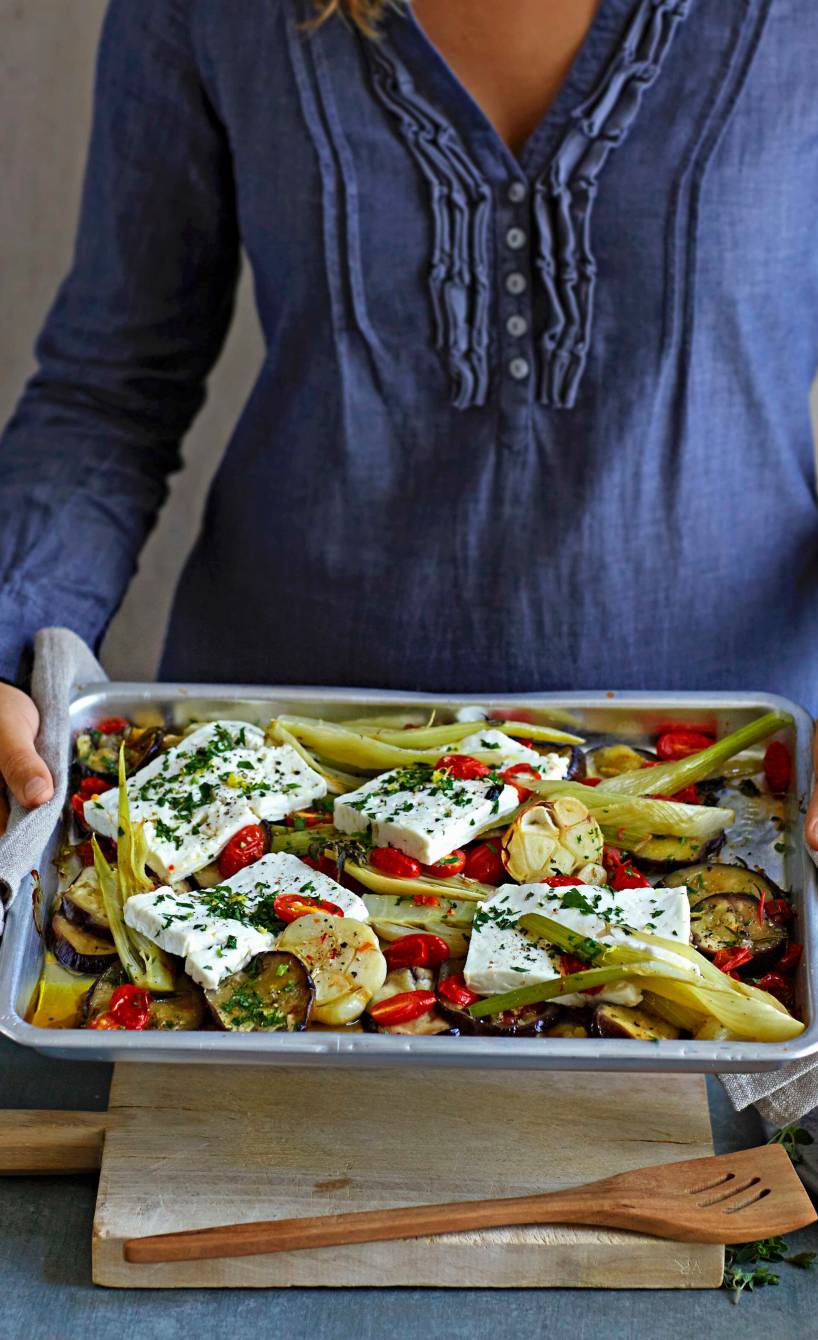 Eine Frau hält ein Backblech mit Auberginen-Fenchel-Gemüse und mit Feta