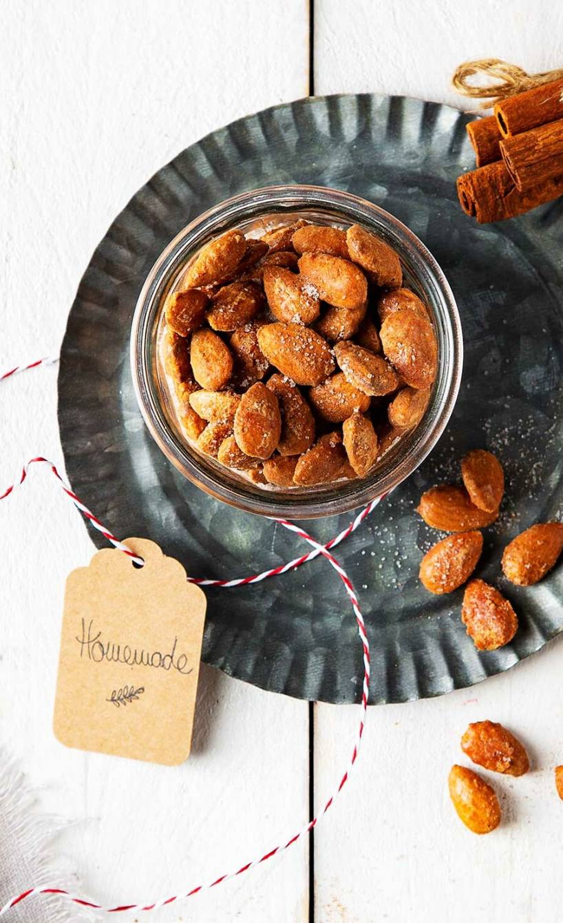 Selbtgemachte gebrannte Mandeln aus der Mikrowelle in einem Glasschälchen auf einem Tisch, daneben Geschenkverpackung