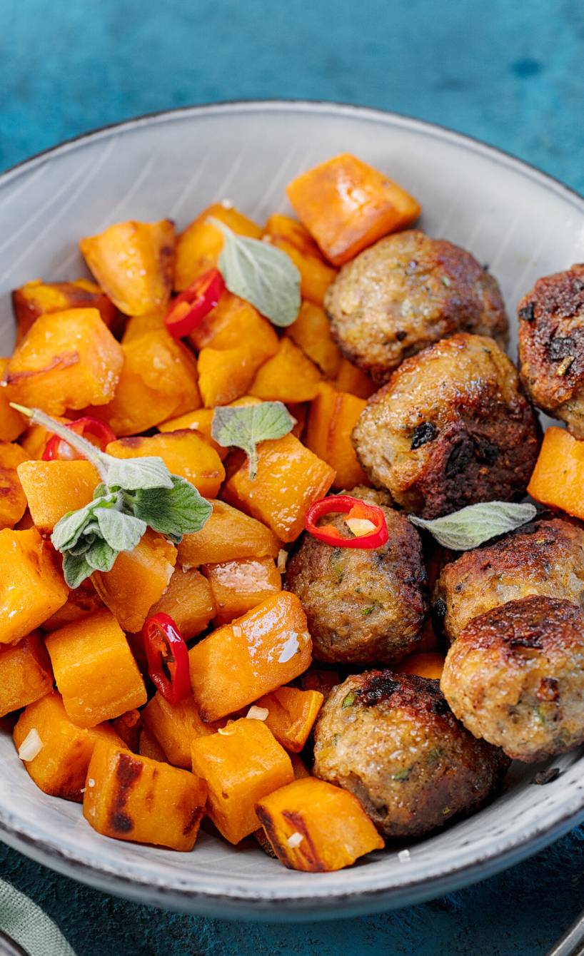 Gebratene Hackbällchen und Süßkartoffelstücke auf einem Teller, daneben eine Schale mit Gewürzen