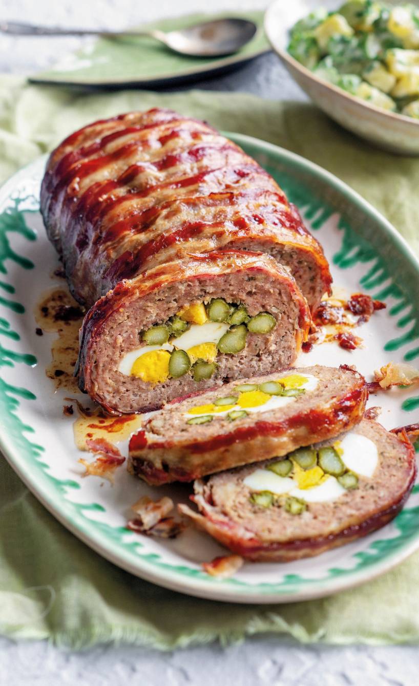 Lamm-Hackbraten im Speckmantel gefüllt mit grünem Spargel und Ei angeschnitten auf einer Servierplatte
