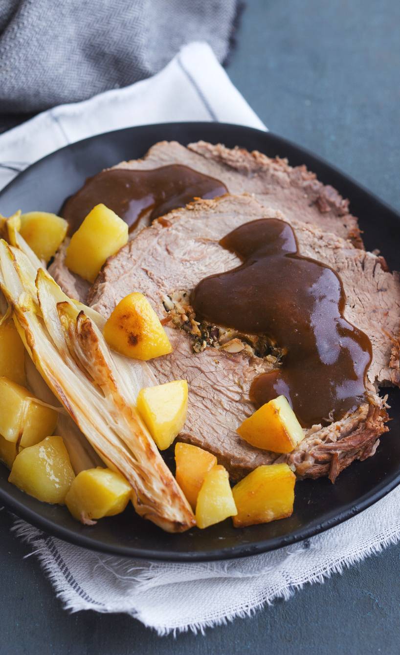 Gefüllter Rinderbraten auf einem Teller, daneben Kartoffeln und Gemüse auf einem Teller