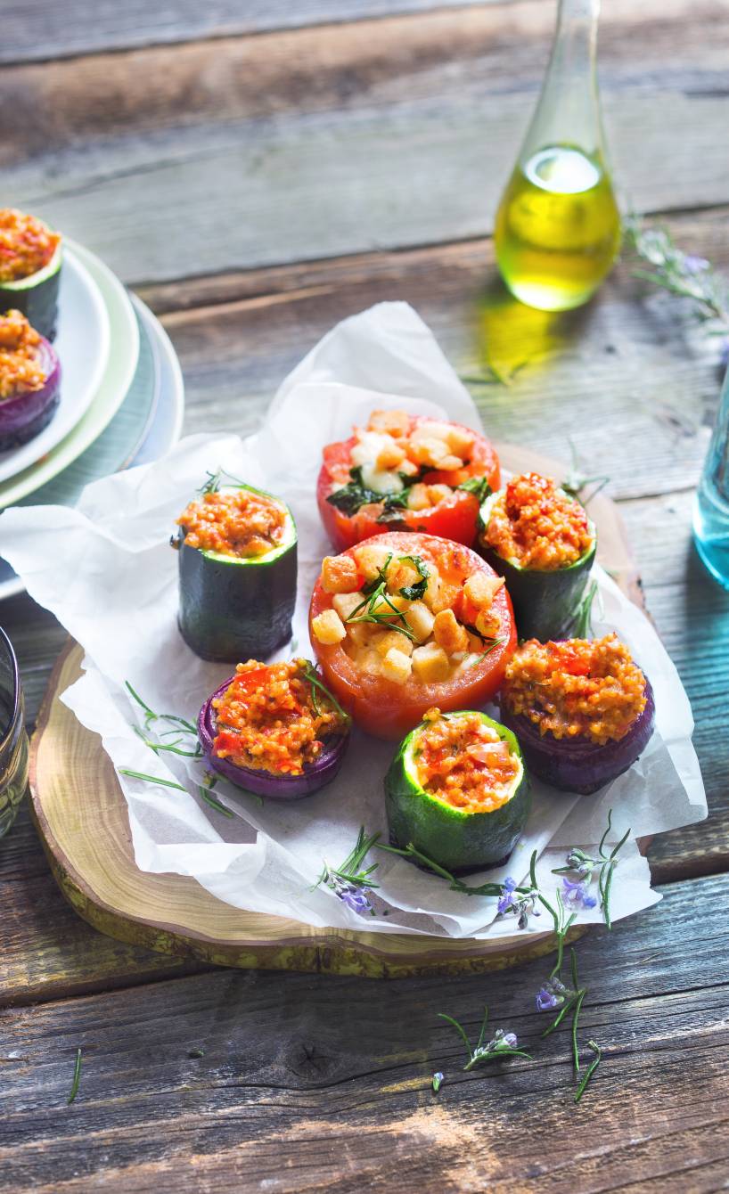Verschiedene Gemüsestücke gefüllt mit Hirsemischung gegrillt auf einem Holzbrett, daneben Olivenöl in einer Flasche