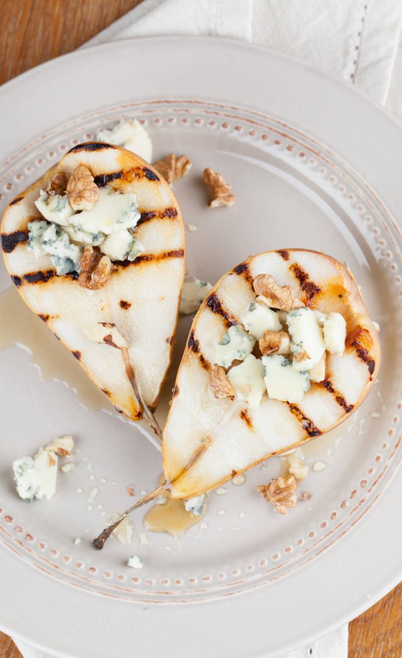 Zwei gegrillte Birnenhälften getoppt mit Gorgonzola und Honig auf einem Teller
