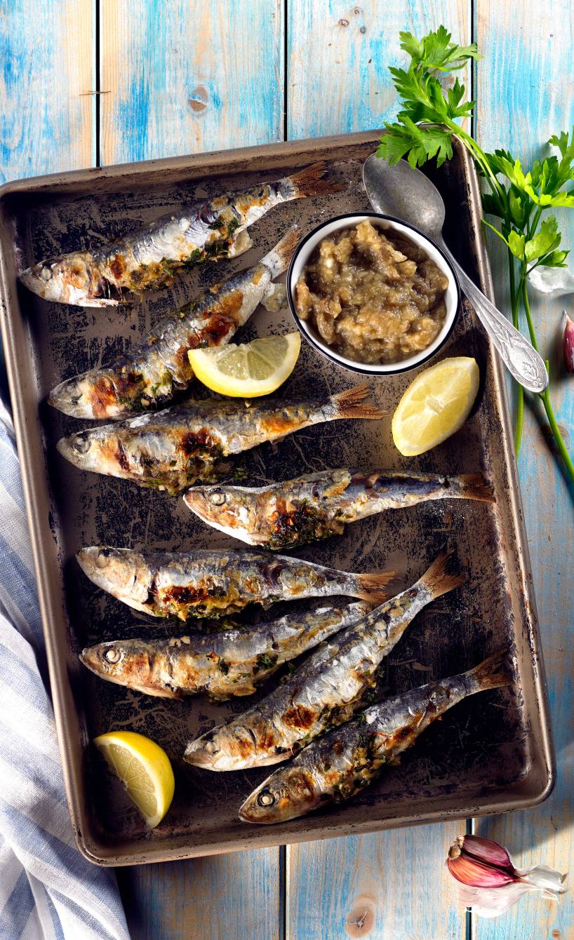 Gegrillte ganze Sardinen auf einer Platte, daneben selbst gemachte Auberginencreme in einer Schale