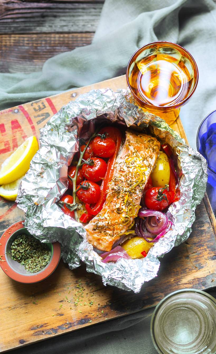 Gegrillte Lachspäckchen mit Gemüse in Alufolie auf einem Tisch