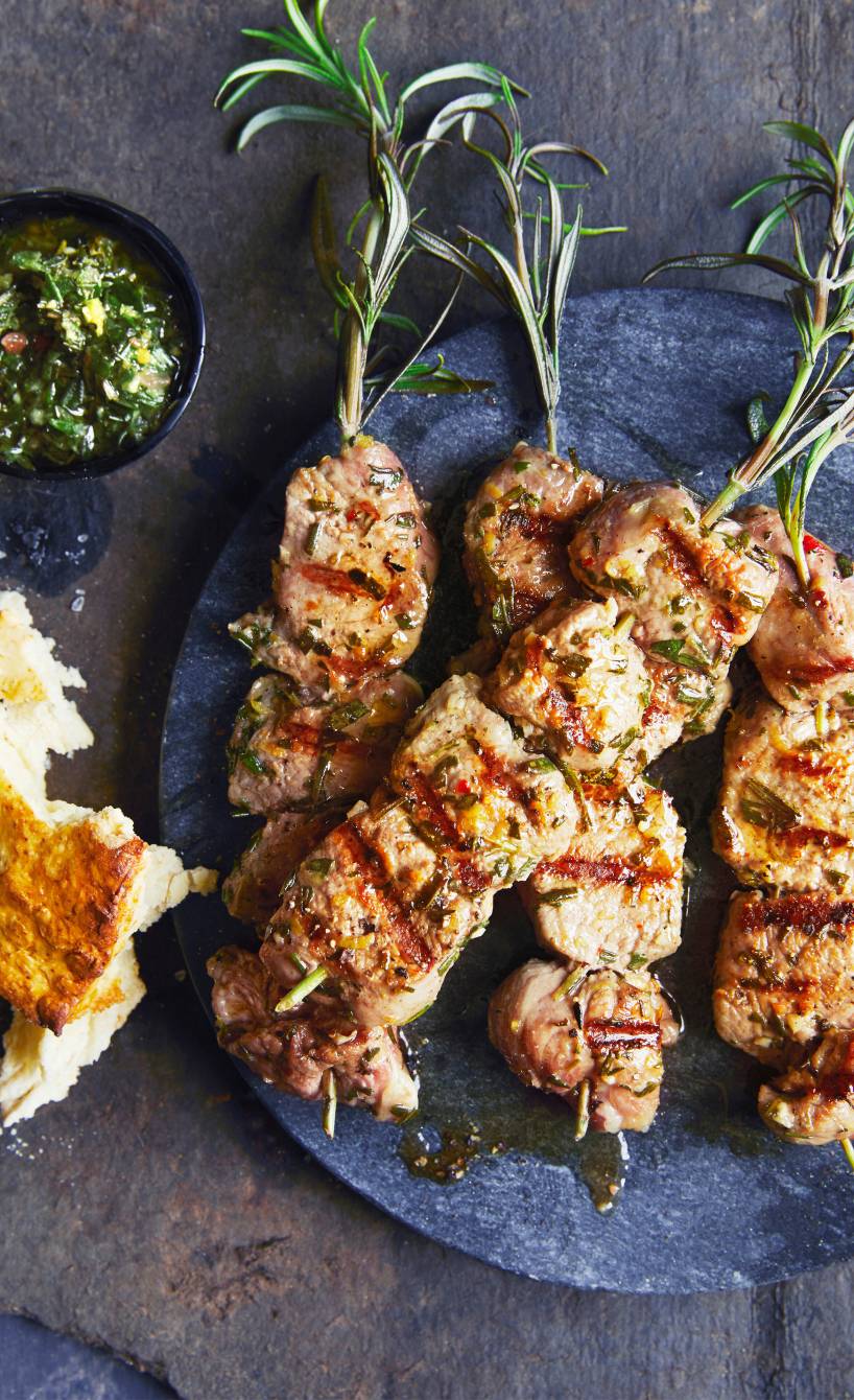 Gegrillte Lammspieße auf einem Teller, darauf kräutersoße, daneben geröstetes Brot