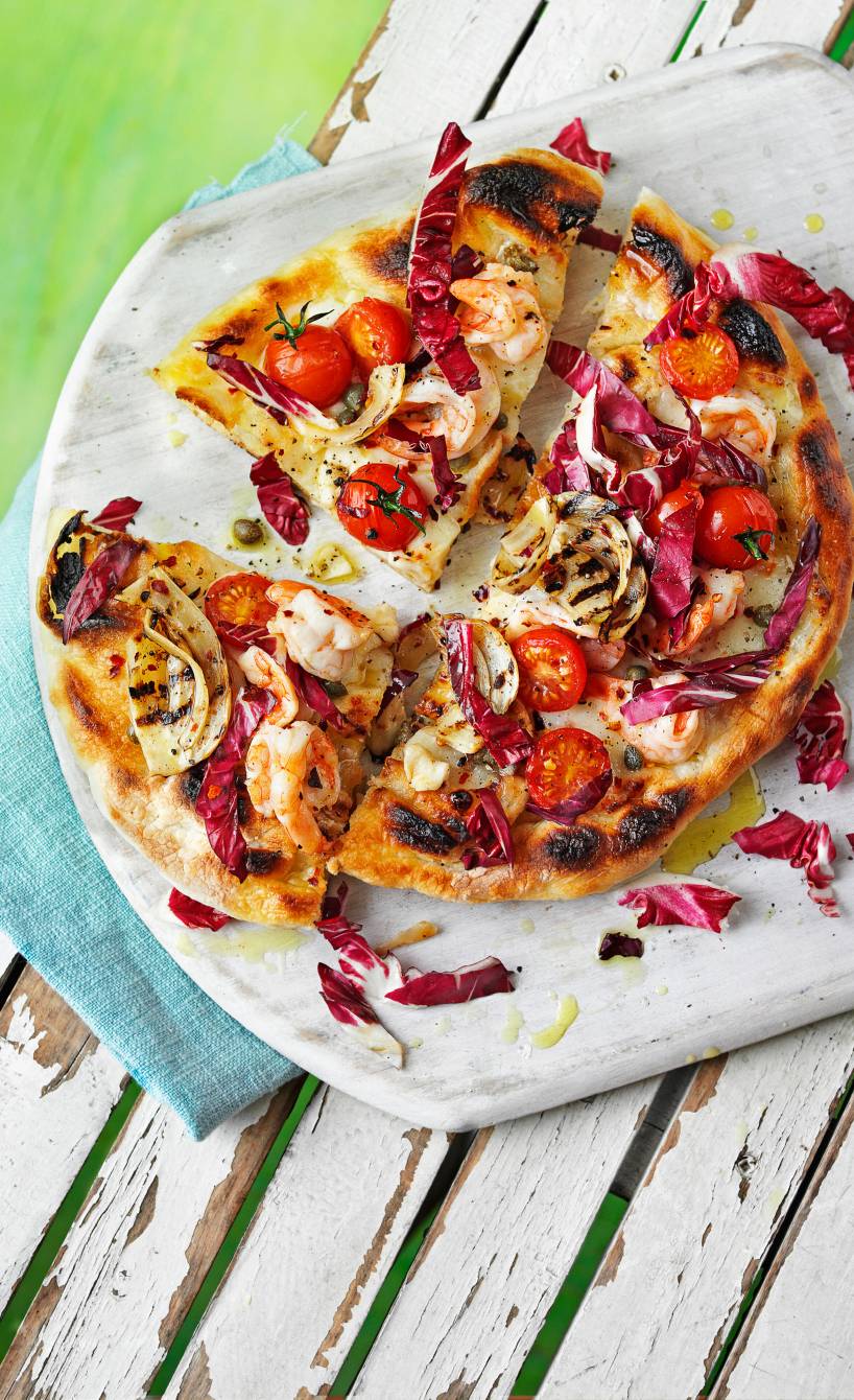 Gegrillte Pizza in Viertel geschnitten auf einem runden Holzbrett