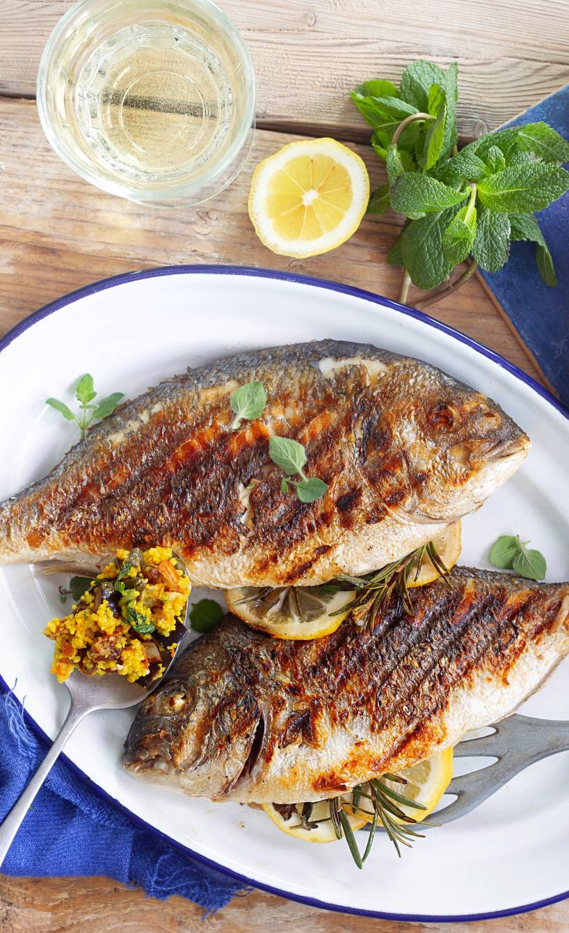 Zwei im Ganzen gegrillte Doraden auf einem Teller, daneben Couscoussalat in einer Schüssel