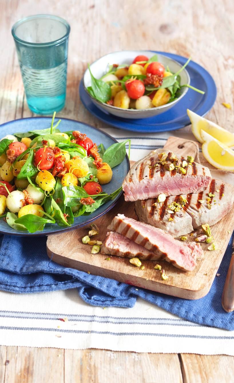 Gegrillte Thunfischsteaks in Dreiecke geschnitten auf einem Teller, daneben Salat mit Gnocchi in einer Schüssel