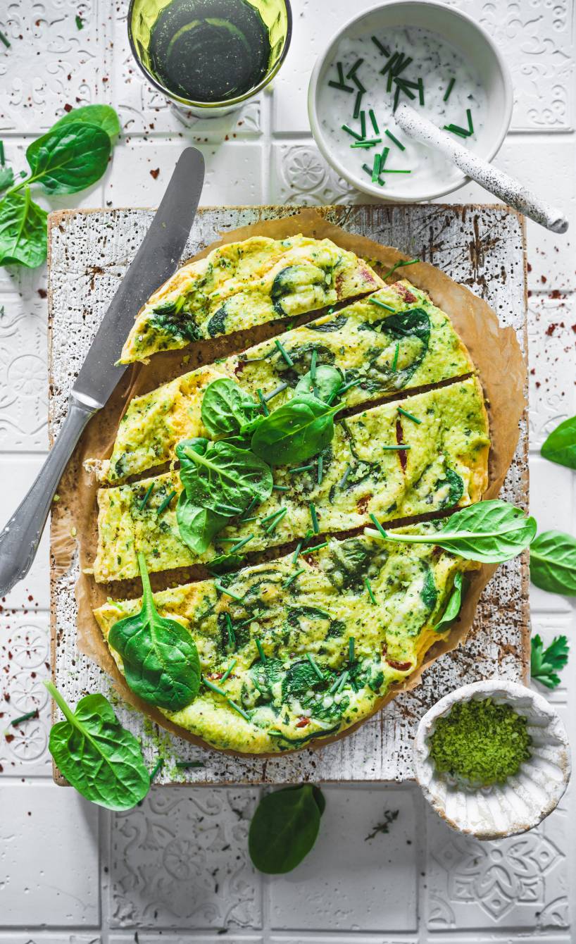  Low Carb Gemüse-Omelett mit Spinat und Parmesan in Streifen geschnitten auf einem Holzbrett, daneben Kräuterdip