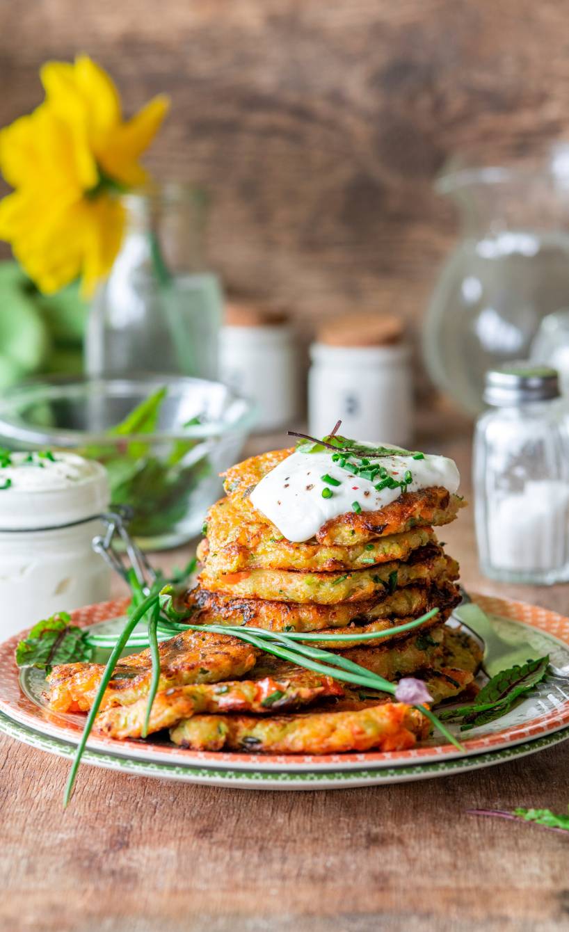 Kartoffel-Gemüse-Bratlinge gestapelt auf einem Teller getoppt mit Quark-Dip und Schnittlauch