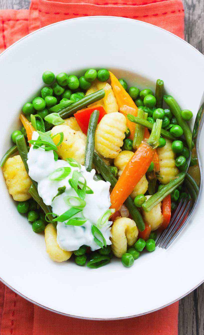 Gnocchi-Gemüse-Pfanne auf einem Teller getoppt mit Joghurt-Dip